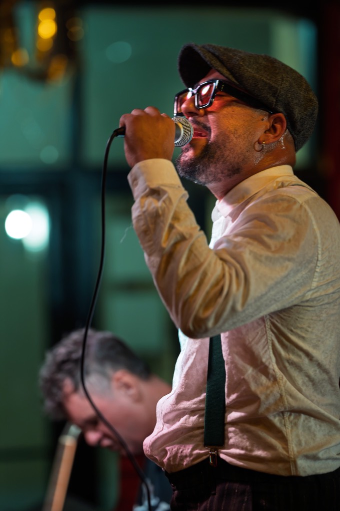 Backdoor Blues Band's singer belting into the mic under warm stage light